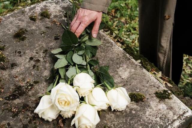 Foto das mãos de um homem depositando rosas brancas em cima de túmulo. A foto ilustra o artigo 10 Estágios do Luto: Lidando com a Perda escrito pelo psicanalista Homero Mônaco para o site Online Psicanalista.