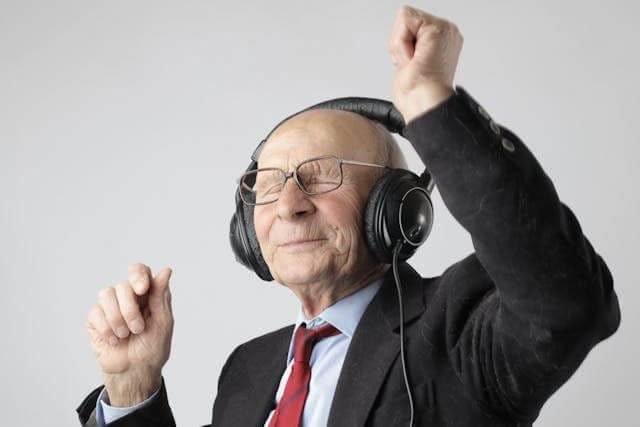 Foto de um homem de uns 60 anos, com fone de ouvido dançando. Ele está de terno e gravata. A foto ilustra o artigo 10 Benefícios da Terapia para a Expansão da sua Consciência Emocional escrito pelo psicanalista Homero Mônaco para o site Online Psicanalista.