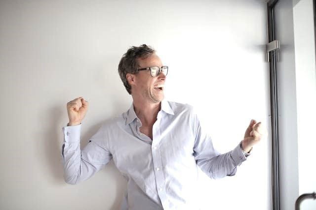 Foto de um homem de camisa branca e óculos vibrando com alguma vitória pessoal dele. A foto ilustra o artigo 10 Maneiras de Alcançar o Empoderamento Pessoal Com a Psicanálise escrito pelo psicanalista Homero Mônaco para o site Online Psicanalista.