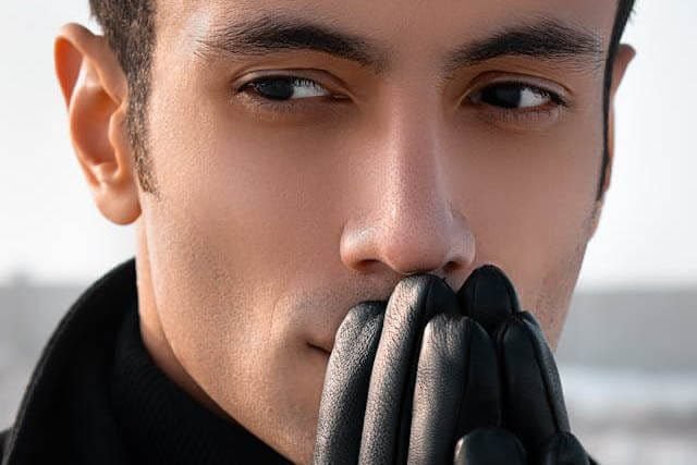 Foto do rosto de um homem com luvas nas mãos. As mãos estão juntas em frente a boca. A imagem ilustra o artigo 6 Maneiras de Explorar os Impactos das Crenças Inconscientes escrito pelo Psicanalista Homero Mônaco para site A Sessão de Terapia.