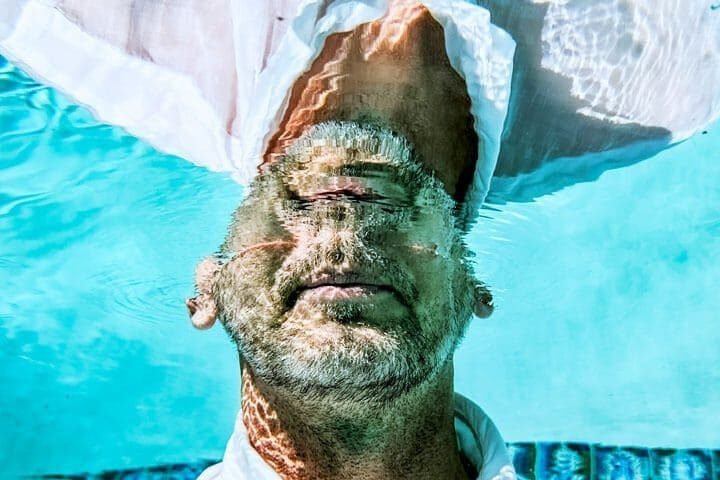 Foto do rosto de um homem enfiando a cabeça em uma piscina, e com a mesma refletindo na água, fazendo referência ao inconsciente. A foto ilustra o artigo Aproveitando o Poder da Mente Inconsciente escrito pelo psicanalista Homero Mônaco para o site Online Psicanalista.