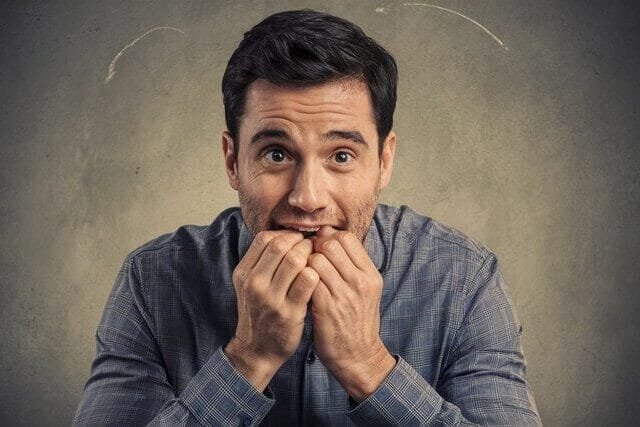 Foto de um homem de aproximadamente 40 anos, com cara ansiosa, mordendo as pontas dos dedos das duas mãos. A foto ilustra o artigo O que é a ansiedade, como controlá-la e quais são seus principais sintomas escrito pelo psicanalista Homero Monaco para o blog do site Online Psicanalista