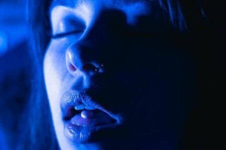 Foto em tons azuis do rosto de perfil de uma jovem com a boca aberta, olhos fechados e um comprimido em sua língua. A foto ilustra o artigo 7 maneiras de como a psicanálise vai te ajudar no tratamento da dependência escrito no blog do psicanalista Homero Mônaco para ao site Online Psicanalista.