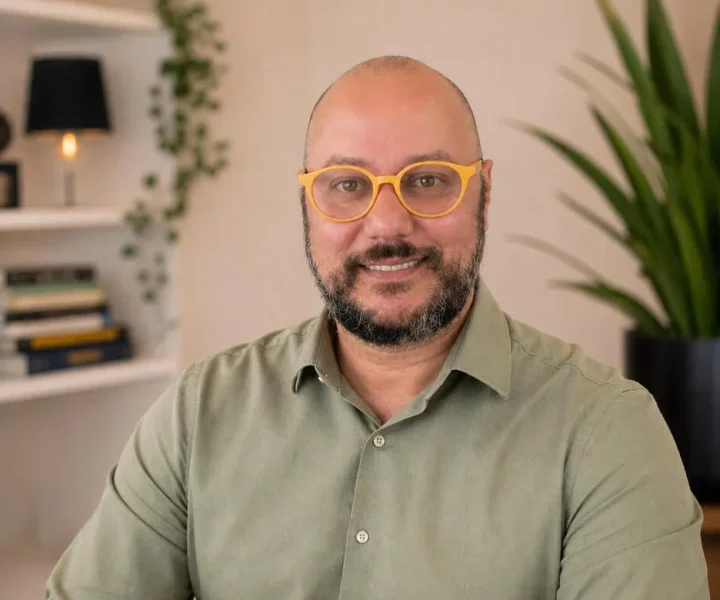 Foto de homem careca, olhos castanhos claros, de barba escura. Óculos Amarelo e camisa verde oliva clara. A foto é do Psicanalista Homero Mônaco, que é o psicanalista que escreve para o blog do Site A Sessão de Terapia e que atende também como psicanalista online.